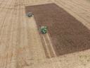 Two green combines harvesting a rectangular patch of standing corn in a harvested field