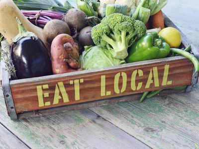 Wooden crate of assorted vegetables with stenciled text "EAT LOCAL"