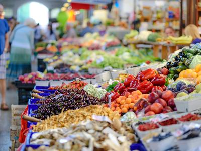 close up of various fruits and vegetables in bins at a farmers market. People walking in the background.