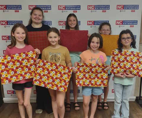 Group holding up placemats that they have sewn.