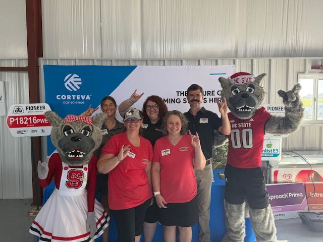 A group of people pose with Mr. and Ms. Wuf, NC State Mascots, at a field day event.