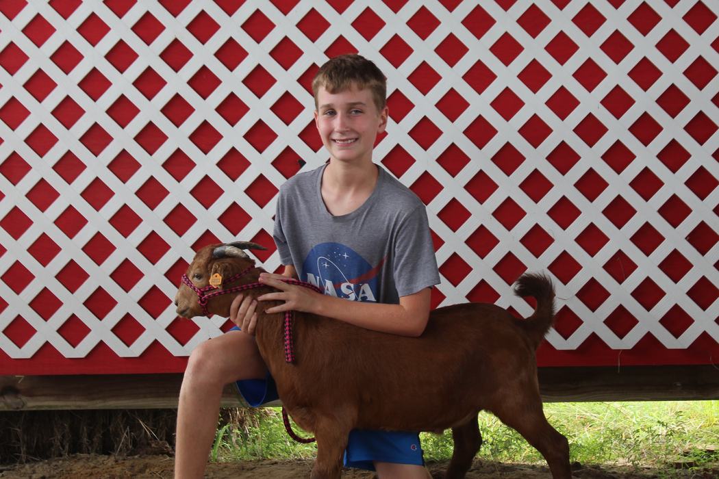 A boy poses with a raised goat.