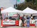 Farmers market tents selling apples and cider; sign "NORTH CAROLINA APPLE CIDER $6"