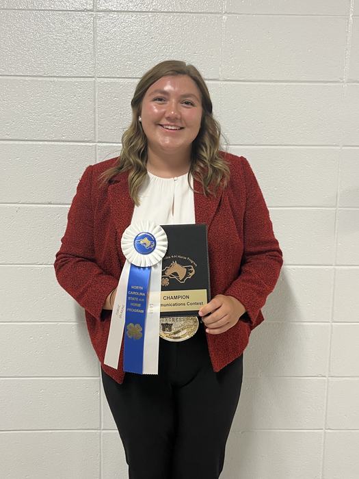 Person holding "Champion Communications Contest" plaque and blue ribbon "North Carolina State 4‑H"