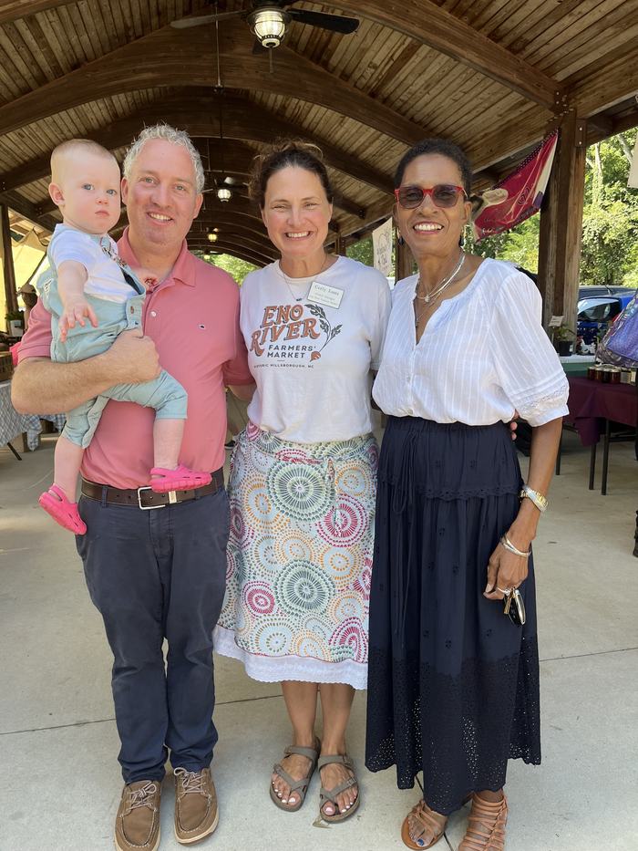 Four people under wooden pavilion at farmers market; shirt reads "ENO RIVER FARMERS MARKET"