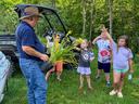 Man holding potted yellow daylilies as four children reach toward them outdoors