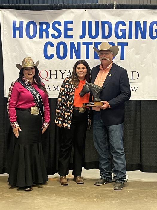 Three people holding a horse-head trophy in front of a banner reading "HORSE JUDGING CONTEST"