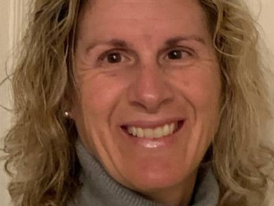 Smiling woman with curly blonde hair wearing a gray turtleneck, close-up.