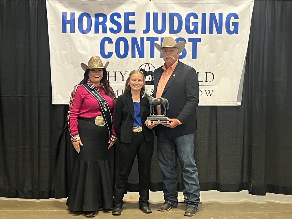 Three people posed holding a horse trophy in front of a banner reading "HORSE JUDGING CONTEST"
