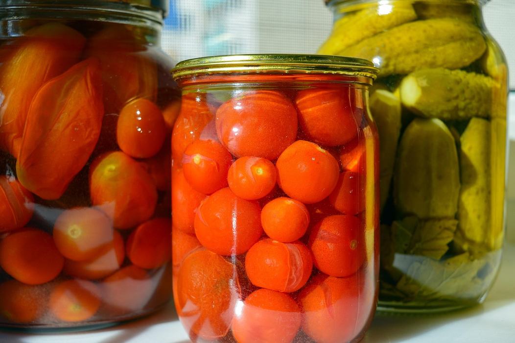 Three glass jars of preserved vegetables: central jar of whole tomatoes, right jar pickles