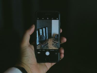 Hand holding a smartphone displaying a photo of two chairs and vertical signs in a dark indoor setting.