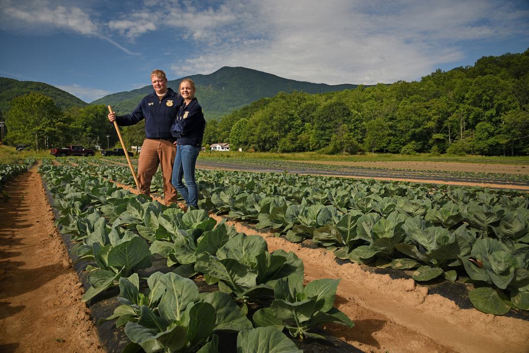 Two farmers standing side by side smiling in a field of collard greens.