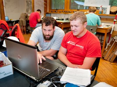 Two people in college of natural resources t-shirts work at a laptop