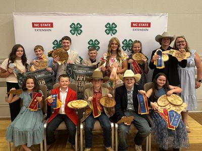 Group of youths holding ribbons and wooden plaques in front of "NC STATE EXTENSION" 4‑H backdrop
