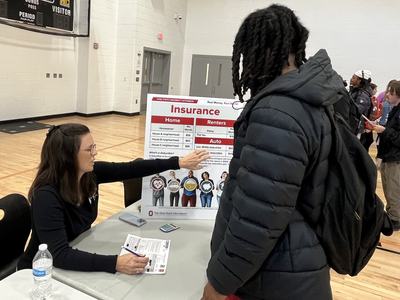 Woman at table points to "Insurance" display board while talking with a student