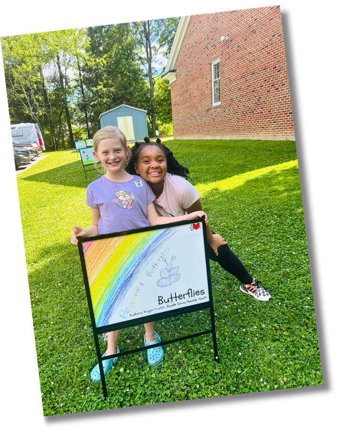 Two girls pose with a StoryWalk sign at their local library