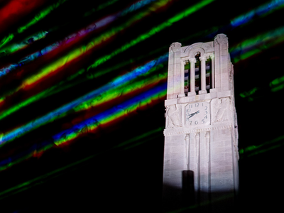 NC State Memorial Belltower at night with colored lasers in foreground.