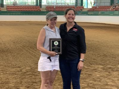 Two women standing in an indoor riding arena holding a 4‑H award plaque
