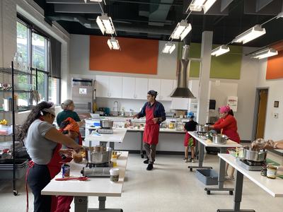 Cooking class with instructor and students wearing aprons and bandanas in kitchen