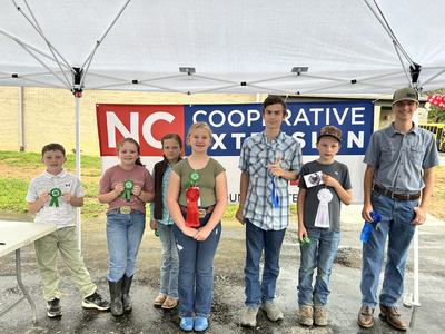 Seven youth under tent holding award ribbons in front of NC Cooperative Extension banner
