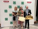 Three people holding bags in front of 4‑H clover backdrop with "NC STATE EXTENSION" text.