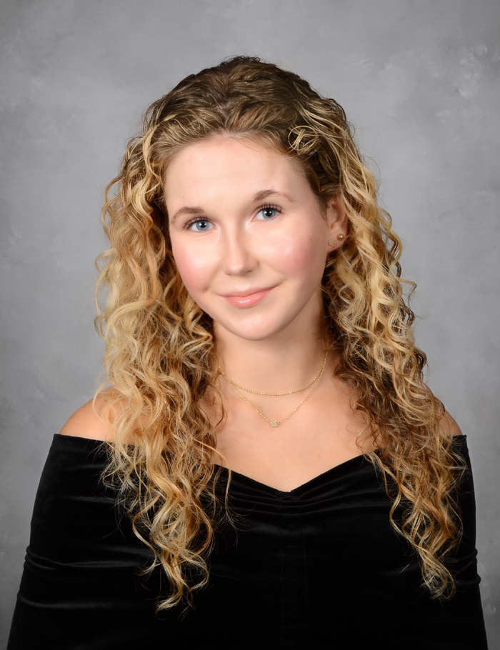 Young women posing in black dress with gray background.