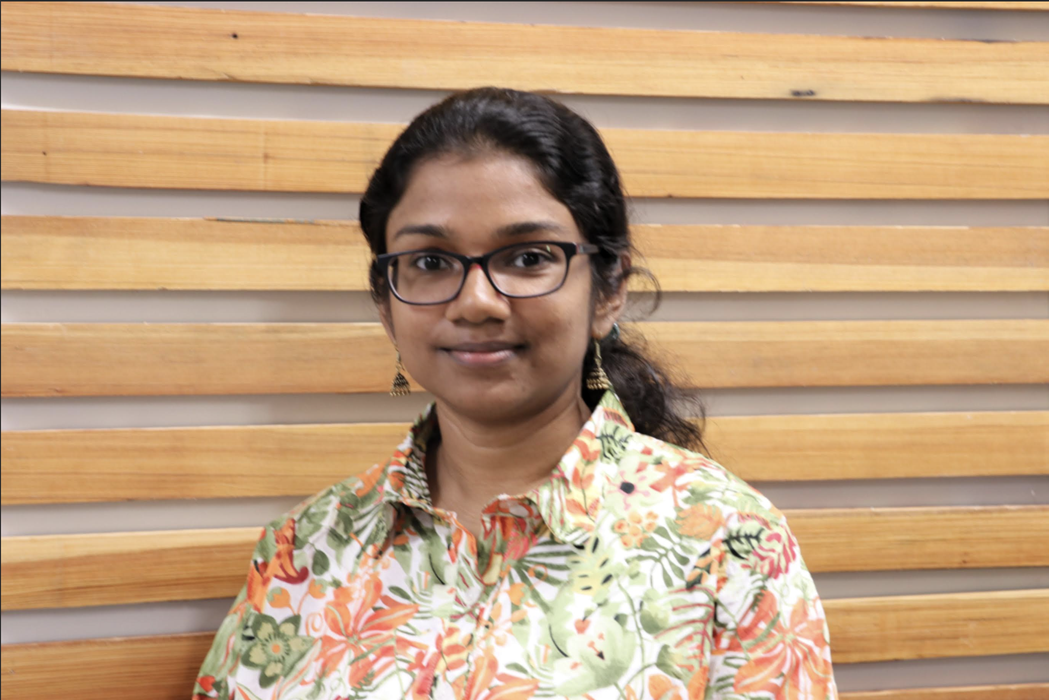 Woman with glasses wearing a floral shirt in front of a wooden slat wall