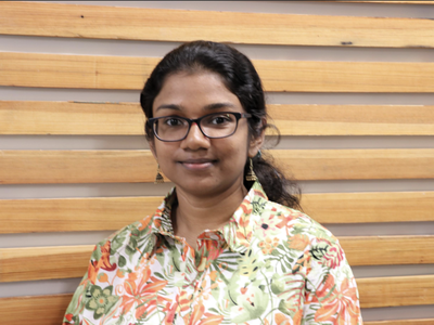 Woman with glasses wearing a floral shirt in front of a wooden slat wall
