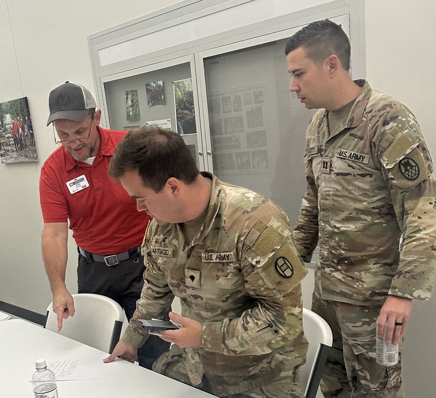 Two U.S. Army soldiers and a man in red pointing at a paper on a table