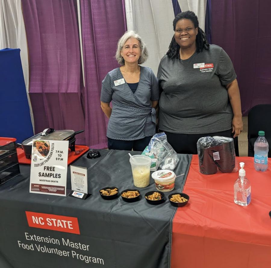 Two volunteers behind NC State Extension Master Food Volunteer Program table with free samples