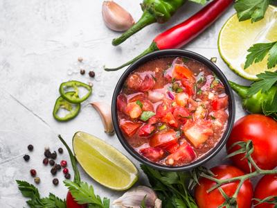 bowl of salsa surrounded by tomatoes, limes, peppers, and cilantros