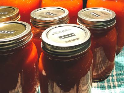 Mason jars of orange tomato sauce on a towel, metal lids labeled "2020"