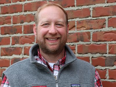 Dr. Ben Chapman, food safety expert with NC State Extension, stands smiling in front of a brick wall.