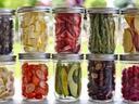 Twelve glass jars filled with assorted dried fruits and vegetables on a windowsill.