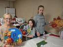Three children holding decorated round fall-themed craft plaques, one with letter "B"