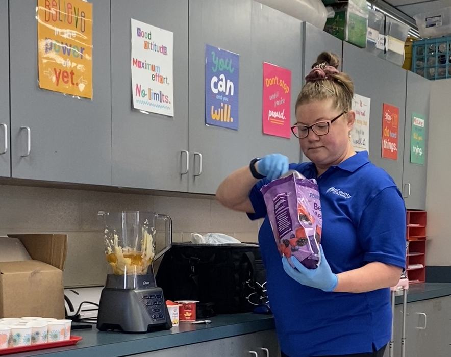 A woman puts a berry medley in a blender to make a smoothie.