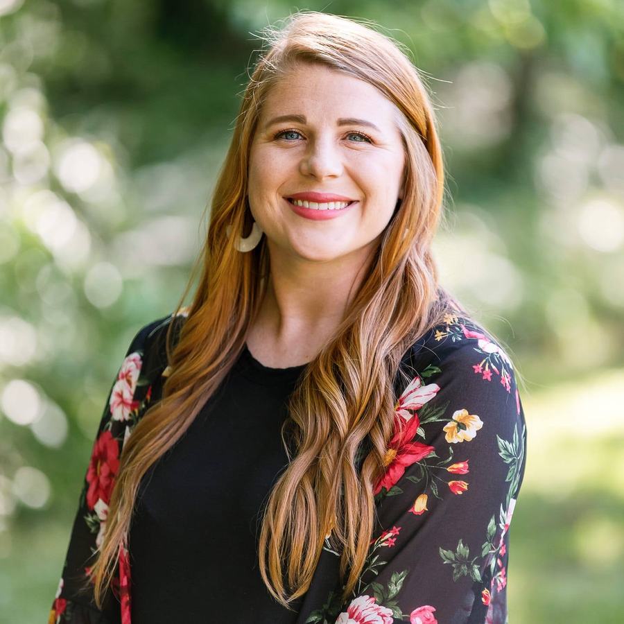 Woman with long red hair in black top and floral cardigan, smiling in outdoor portrait
