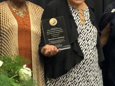 Two women standing side by side, one holding a glass award plaque.