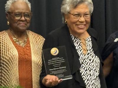 Two women standing side by side, one holding a glass award plaque.