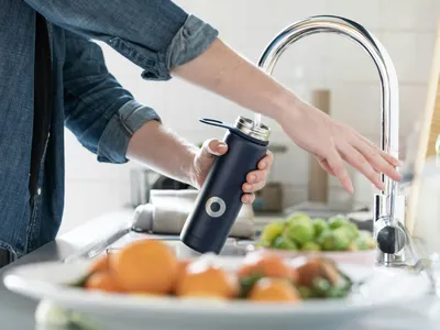 Person filling water bottle at sink.