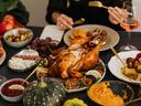 Photo of a table of fall decor and various foods. A roasted turkey sits at the center of the table. In the background you see the hands of someone holding eating utensils over a plate.