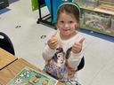 a little girl giving a thumbs up sign with a pumpkin life cycle mat on her desk