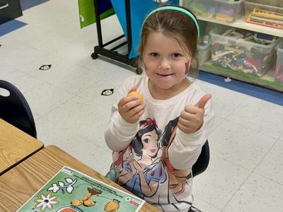 a little girl giving a thumbs up sign with a pumpkin life cycle mat on her desk