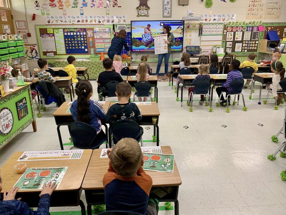 2 female adults in front of students with posterboards with pumpkins