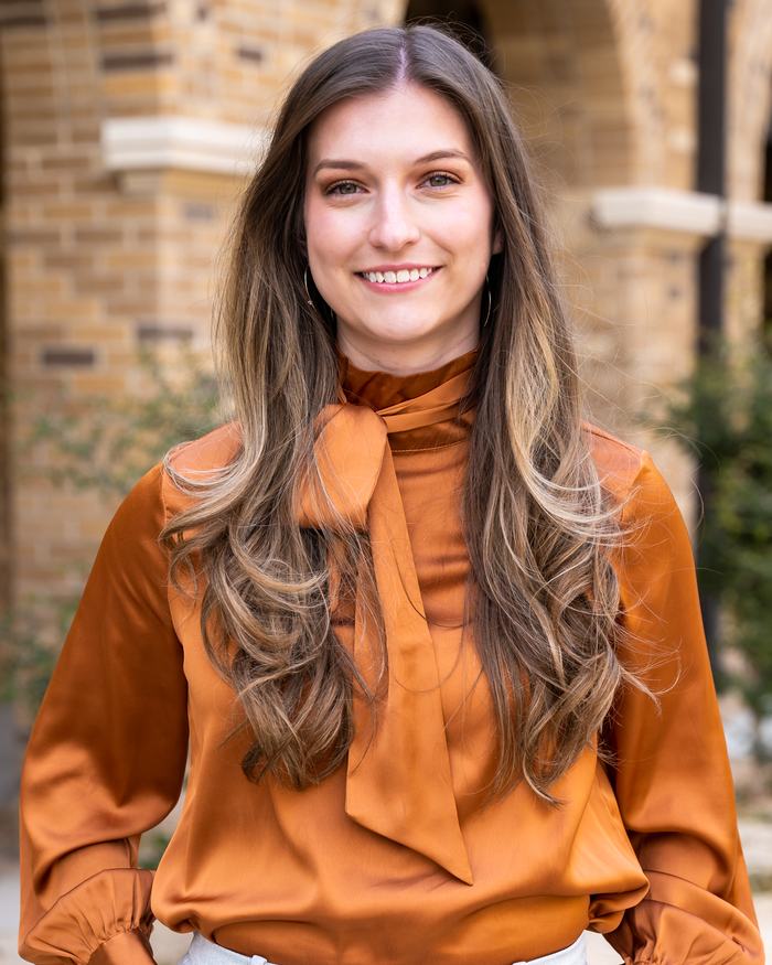 Woman wearing rust-colored blouse standing outdoors in front of brick building