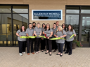 A group of eleven staff members in matching gray shirts stand outside the "Allen Ray McNeill Education & Resource Center" building, holding a wide green ribbon during a ribbon-cutting ceremony.