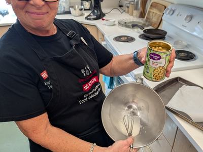 Person holding can labeled "Organic Garbanzo Beans" over mixing bowl with whisk