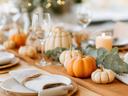 Autumn table setting with small pumpkins, eucalyptus, lit candle, wine glasses, napkins