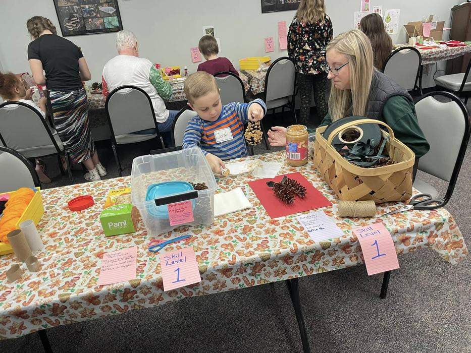 Caldwell County 4-H Junior Leader Macy Sparks helps 4-H'er Jonah Prestwood make a pinecone ornament.