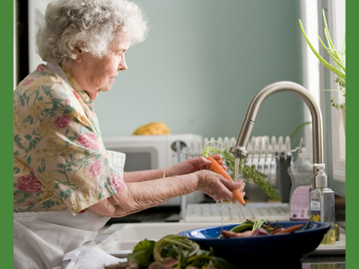 Older person washing carrots under a kitchen faucet